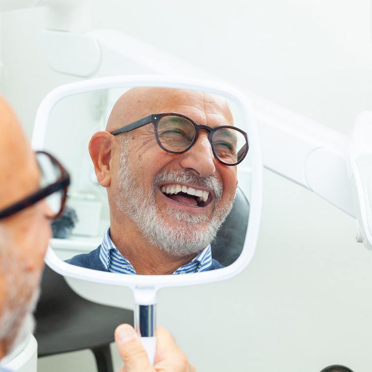 Happy senior dental patient reflected in hand mirror