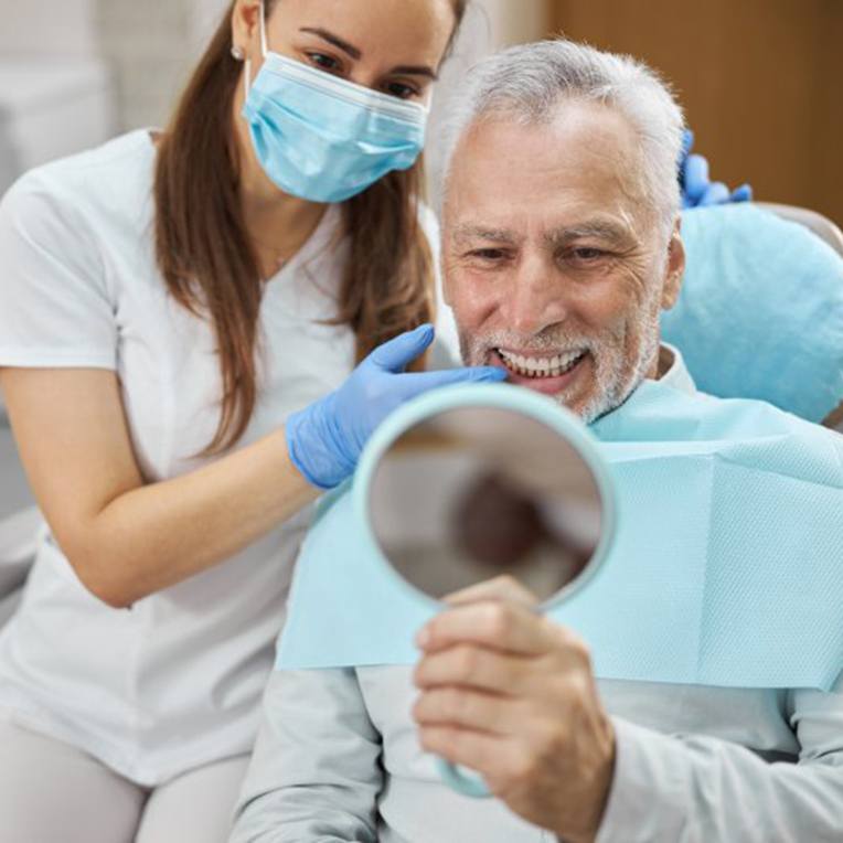 Dentist pointing out patient’s teeth as he looks in a small mirror