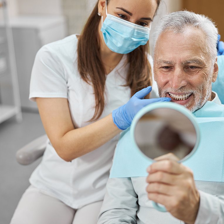 man smiling while holding dental mirror 