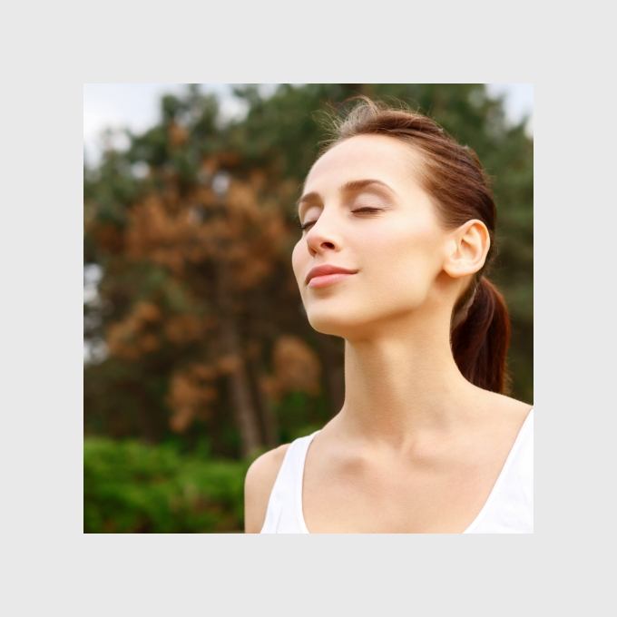 Woman closing her eyes and smiling outdoors with trees in background