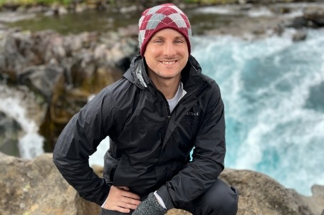 Smiling Doctor Young in jacket and beanie with waterfall in background